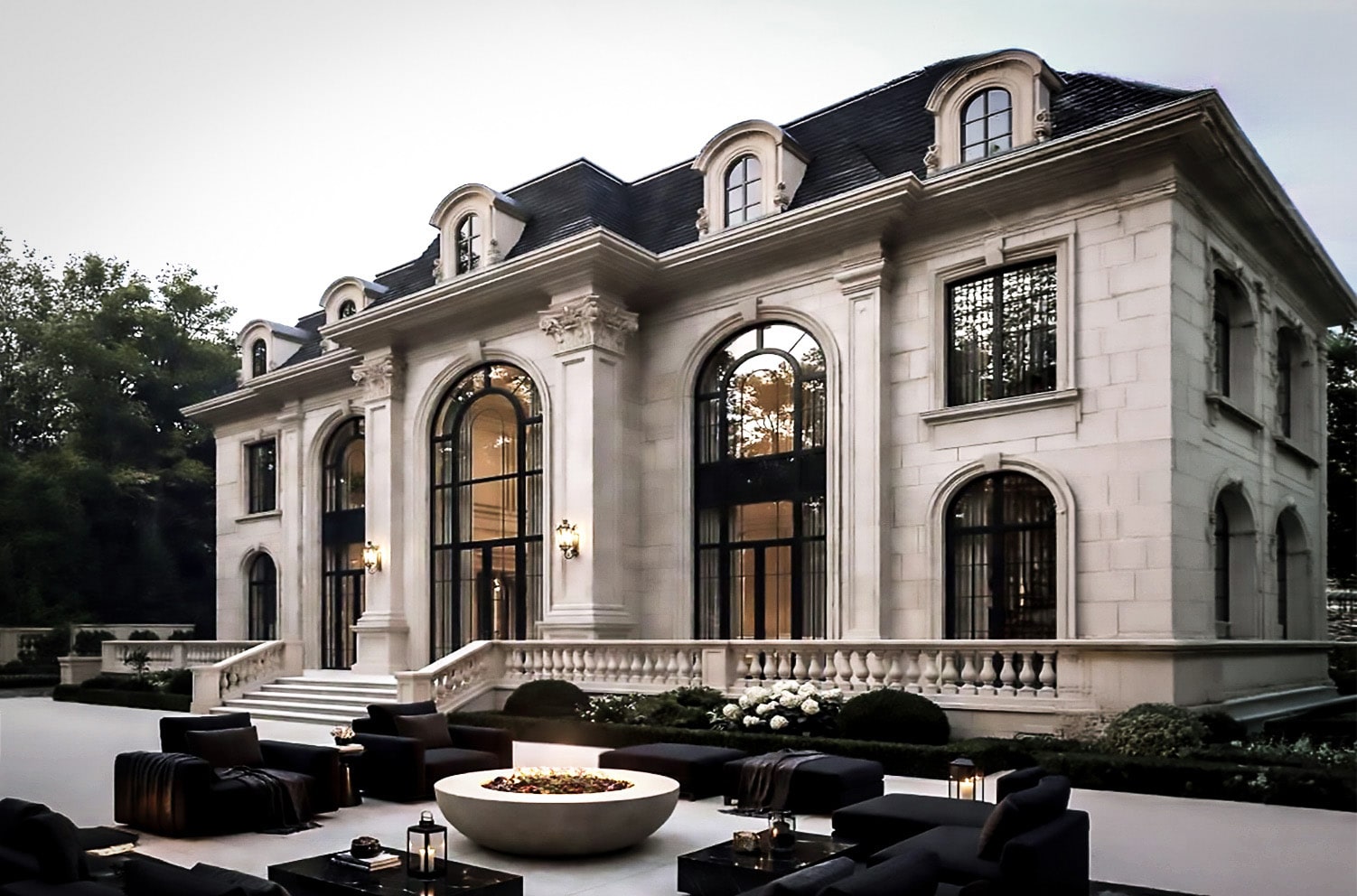 Stone mansion at dusk with a patio fire pit and outdoor lounge furniture