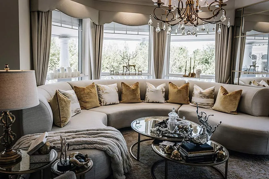 Living room with curved cream sofa, gold cushions and mirrored coffee tables