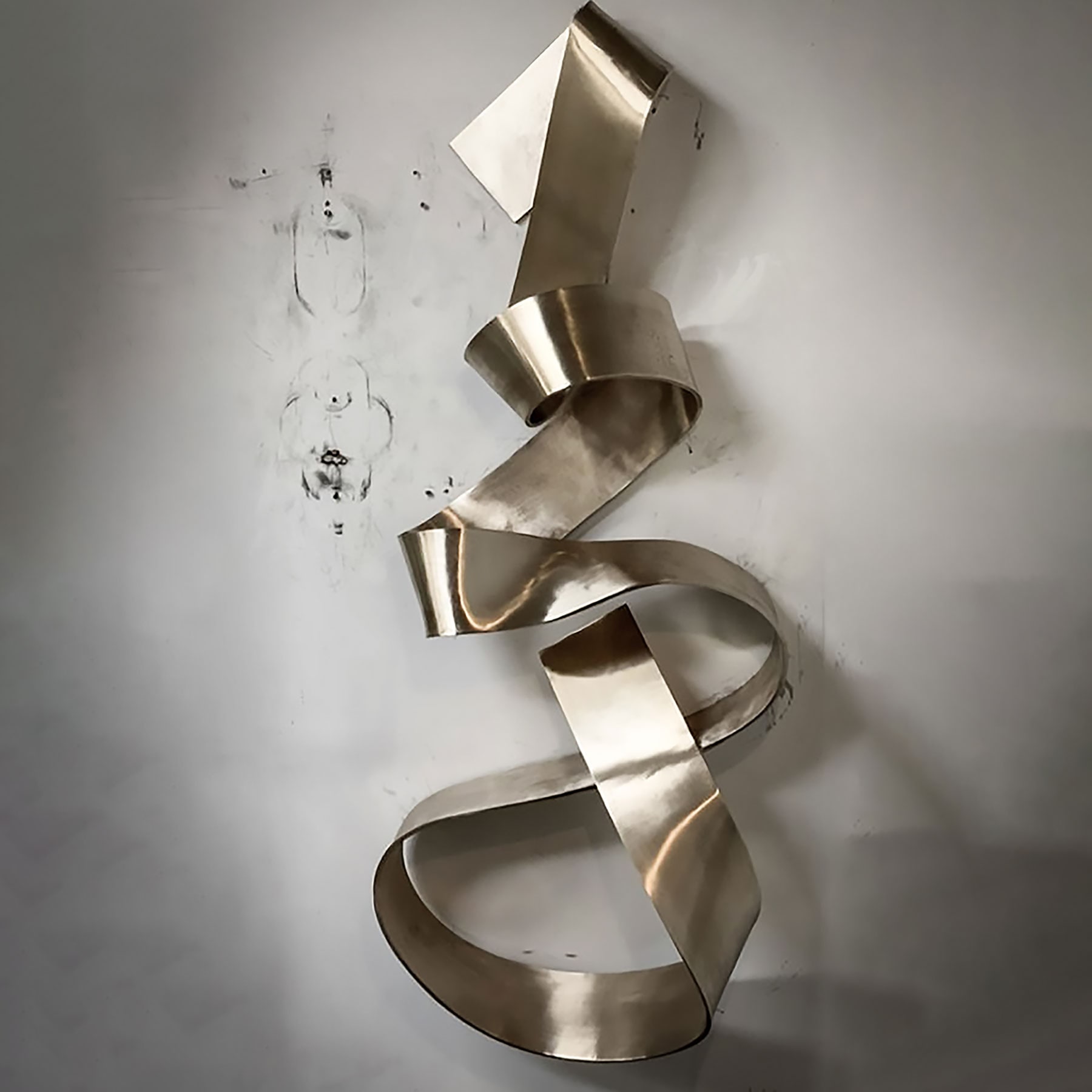 Coiled polished metal ribbon sculpture on a light wall