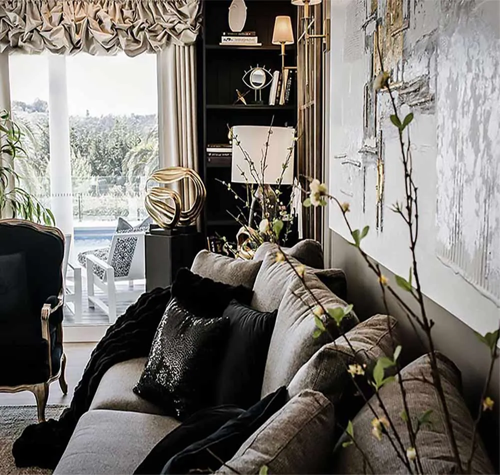 Living room with grey sofa, sequined cushions, black bookshelf and gold artwork